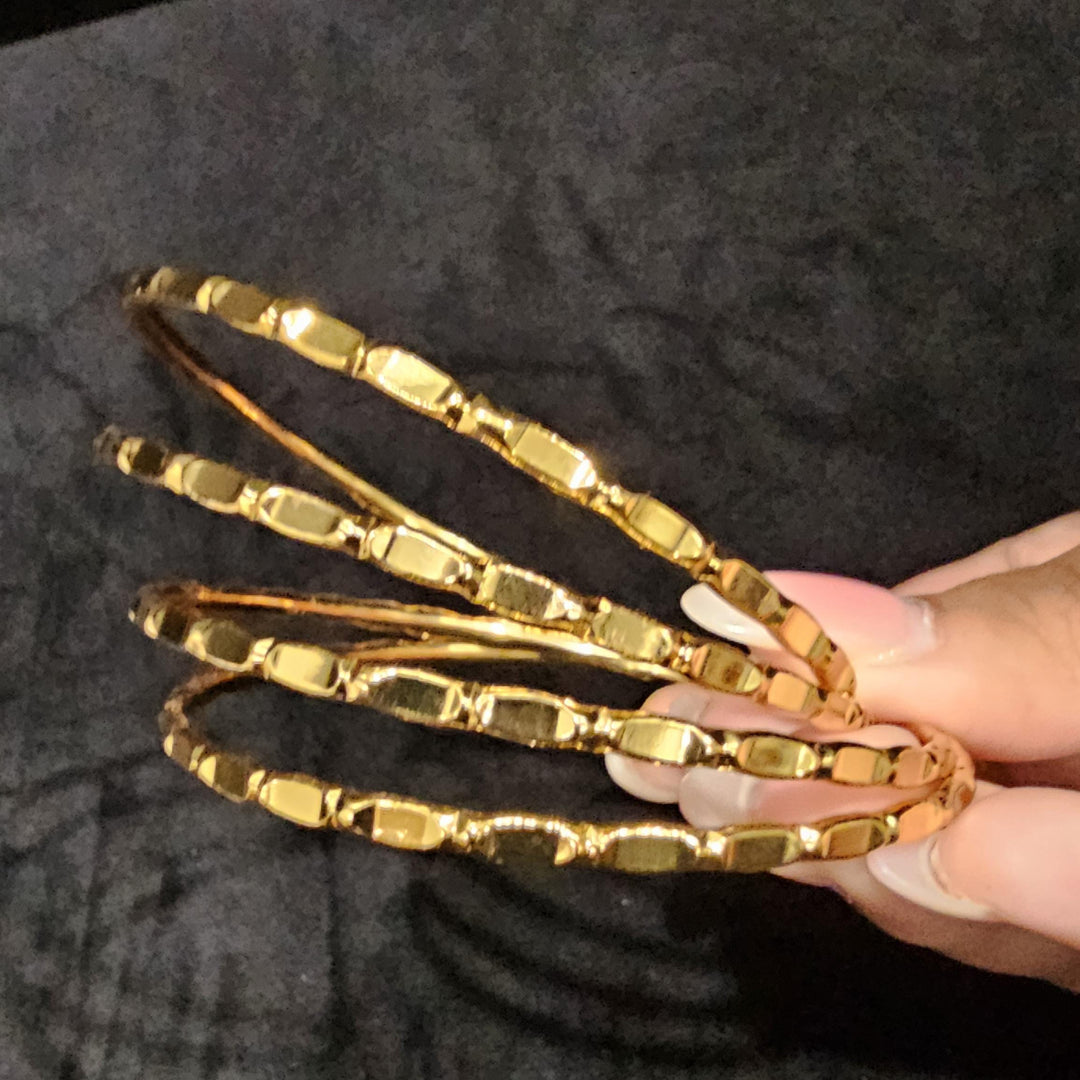 May include: Four gold bangles with a textured design. The bangles are stacked on top of each other.