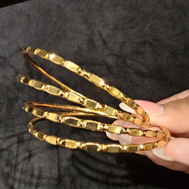 May include: Four gold bangles with a textured design. The bangles are stacked on top of each other.